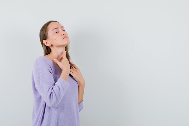 Young lady touching her neck in casual shirt and looking peaceful 