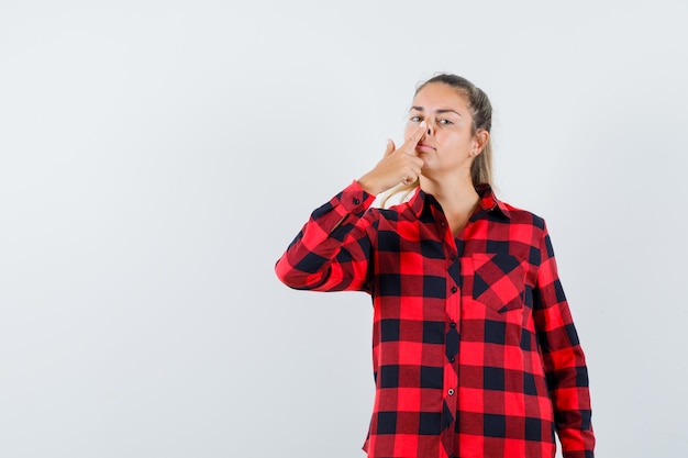 Young lady touching her nose with finger in checked shirt and looking cute