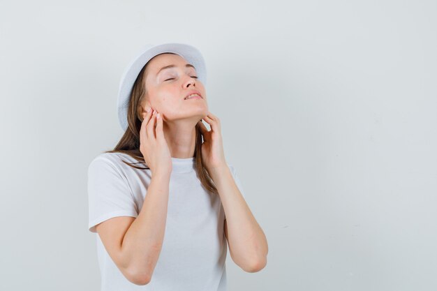 Young lady touching her skin in white t-shirt hat and looking peaceful  