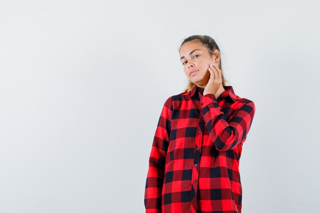 Young lady touching skin on her cheek in checked shirt and looking delicate