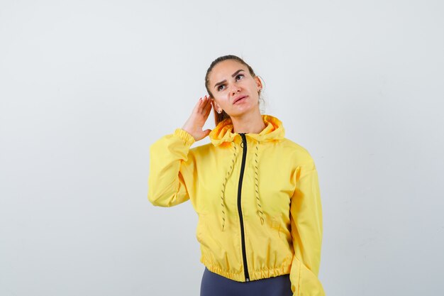 Young lady in tracksuit with hand behind ear and looking curious , front view.