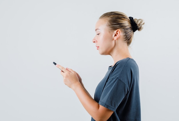 灰色のTシャツで携帯電話で入力する若い女性