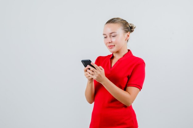 Young lady using mobile phone and smiling in red t-shirt