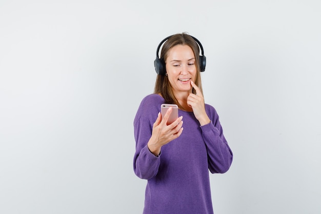 Девушка в фиолетовой рубашке, глядя на мобильный телефон и улыбаясь, вид спереди.