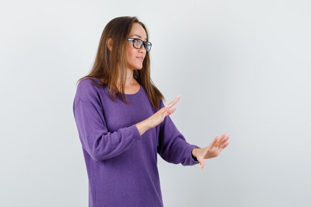 Young lady in violet shirt making slow down gesture and looking curious , front view.