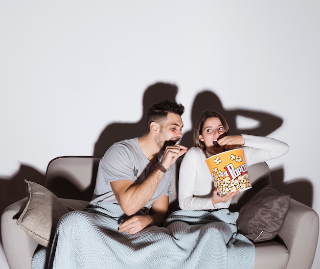 Young lady watching TV and eating popcorn near guy on settee