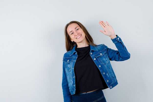 Young lady waving hand for greeting in blouse, jacket and looking jolly