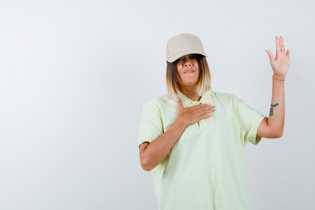 Young lady waving hand for greeting in t-shirt, cap and looking hesitant , front view.