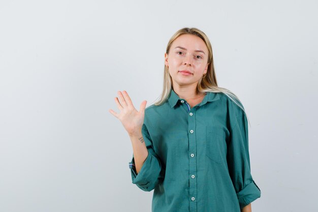 Young lady waving hand to say goodbye in green shirt and looking confident