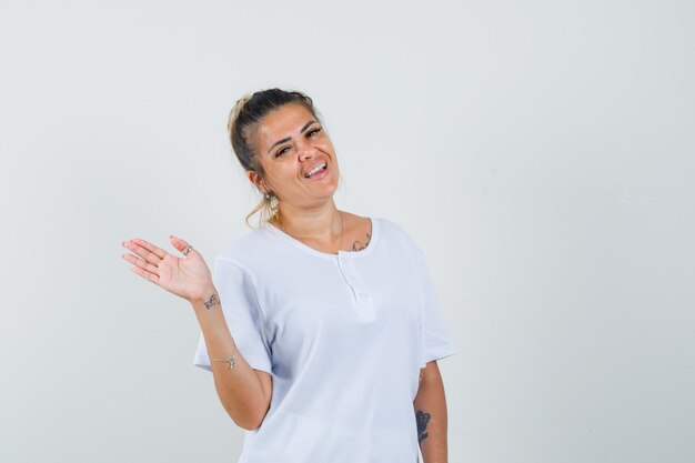 Young lady waving hand to say goodbye in t-shirt and looking cheerful 