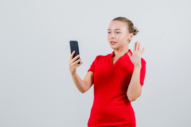 Young lady waving hand on videocall in red t-shirt