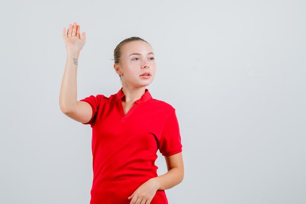 Young lady waving hand while looking away in red t-shirt