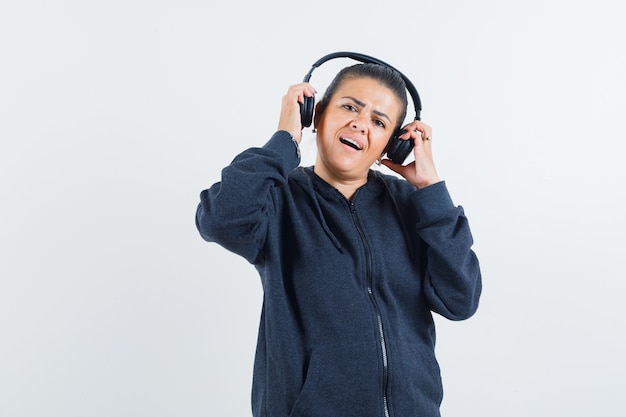 Young lady wearing earphones in jacket and looking glad. front view.