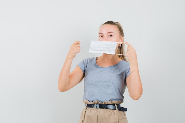 Young lady wearing medical mask in t-shirt and pants and looking careful