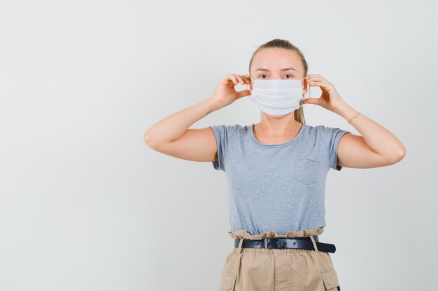 Young lady wearing medical mask in t-shirt and pants and looking careful