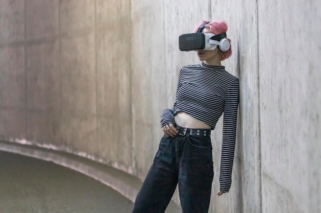 VR 세트를 착용하고 벽에 기대어 있는 젊은 여성