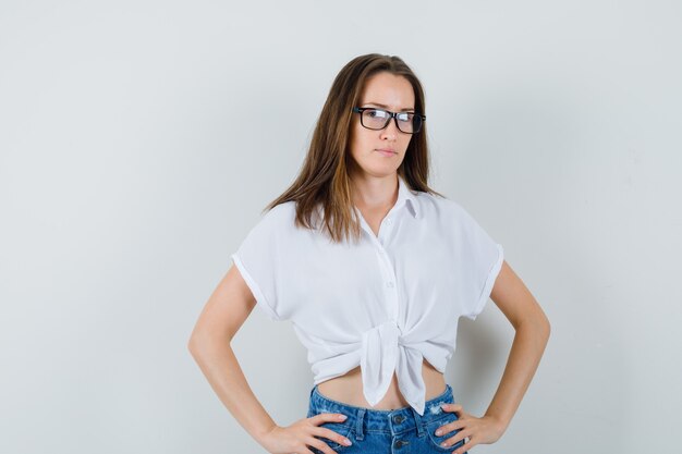 Young lady in white blouse,glasses holding hands on her waist , front view.