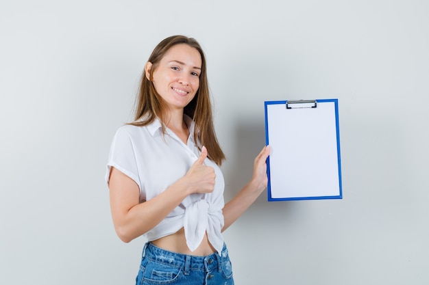 Young lady in white blouse holding blank clipboard while thumb up , front view.