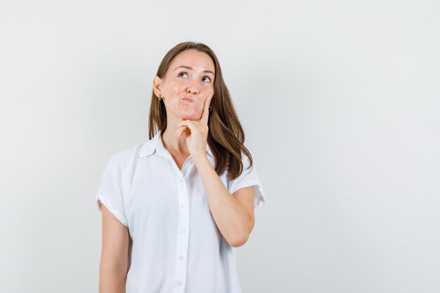 Young lady in white blouse holding hand on her cheek and looking thoughtful