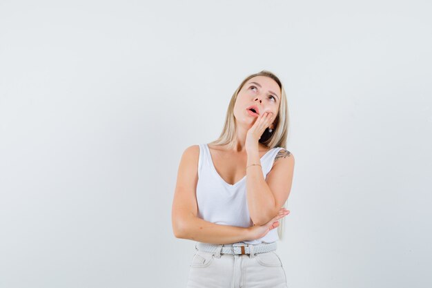 Young lady in white blouse looking away while leaning at her hand and looking thoughtful