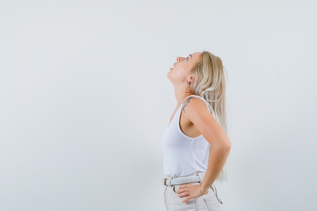 Young lady in white blouse looking up while holding hands on waist and looking focused . space for text