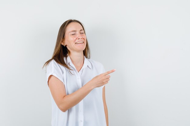 Young lady in white blouse pointing aside and looking positive