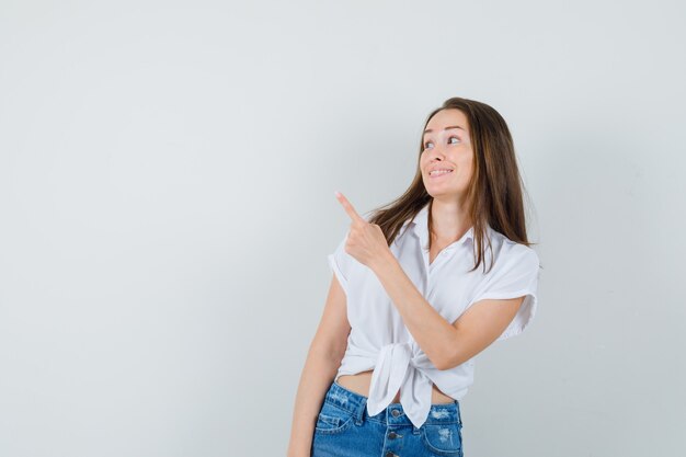 Young lady in white blouse pointing back and looking jojoyus , front view. space for text