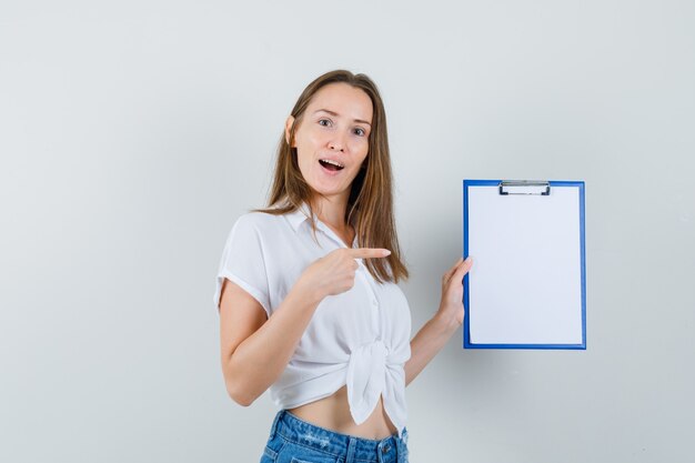 Young lady in white blouse pointing to blank clipboard , front view.