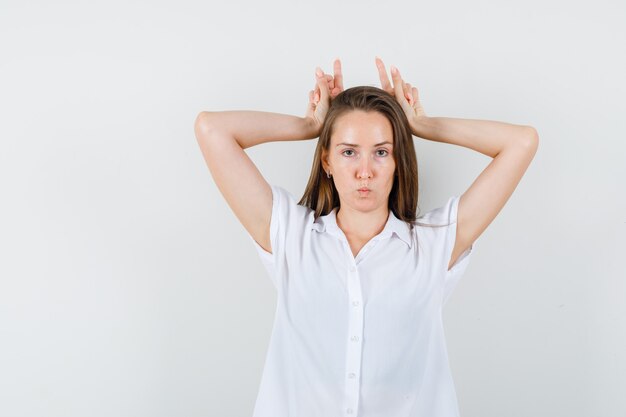 Young lady in white blouse showing bunny gesture and looking weird