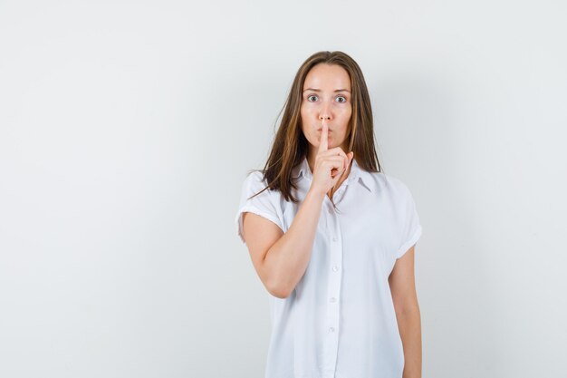 Young lady in white blouse showing silence gesture and looking strict