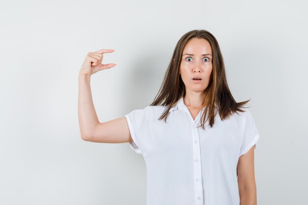 Young lady in white blouse showing small size sign and looking scared