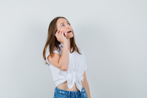 Young lady in white blouse talking on phone and looking focused , front view.