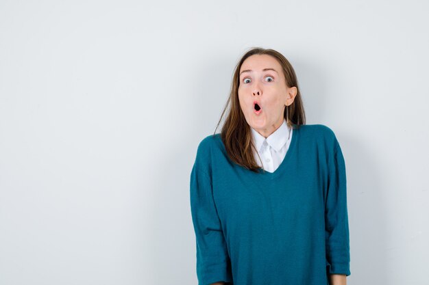 Young lady in white shirt, sweater looking shocked , front view.