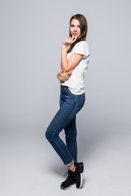 Young lady in white t-shirt and blue jeans give an air kiss in front of white studio background