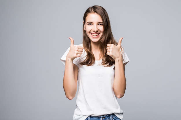 Young lady in white t-shirt and blue jeans shows thumbs up sing in front of white studio background