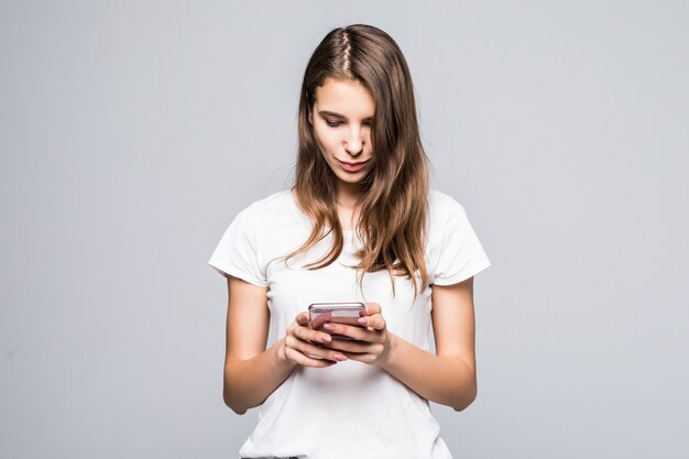 Молодая дама в белой футболке и синих джинсах остается с телефоном на белом фоне студии