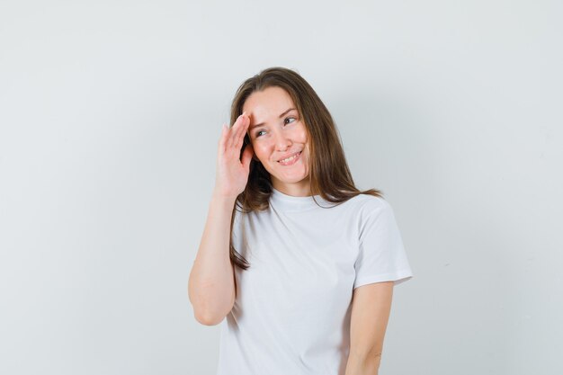 Young lady in white t-shirt looking aside behind hand and looking ashamed  