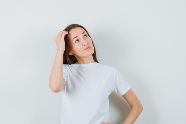 頭をかいて思慮深く見える白いTシャツの若い女性