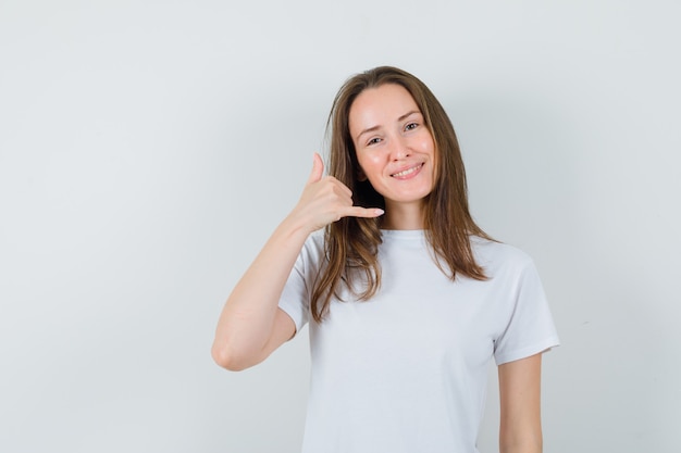 Young lady in white t-shirt showing phone gesture and looking helpful  