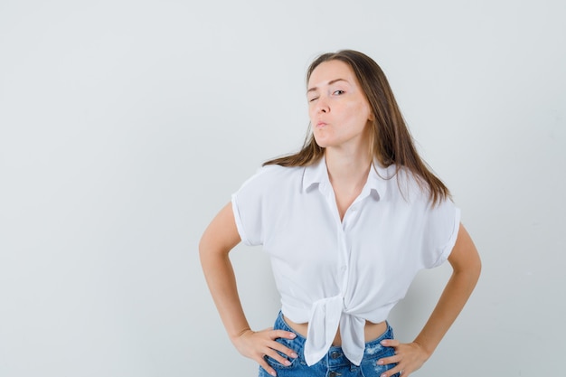 Foto gratuita giovane donna che fa l'occhiolino mentre fa il broncio con le labbra in camicetta bianca e sembra concentrata. vista frontale.