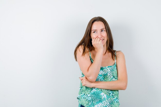 Young lady with hand on cheek in blouse and looking cute. front view.