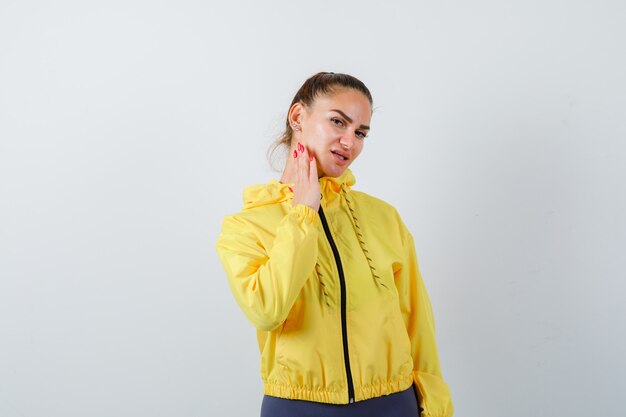 Young lady with hand on cheek in yellow jacket and looking careful , front view.