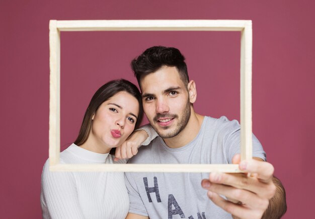 Young lady with hand on shoulder of positive guy holding photo frame