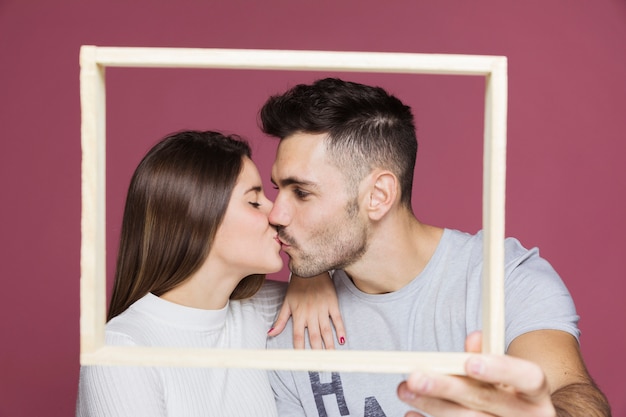 Young lady with hand on shoulder of positive guy kissing and showing photo frame