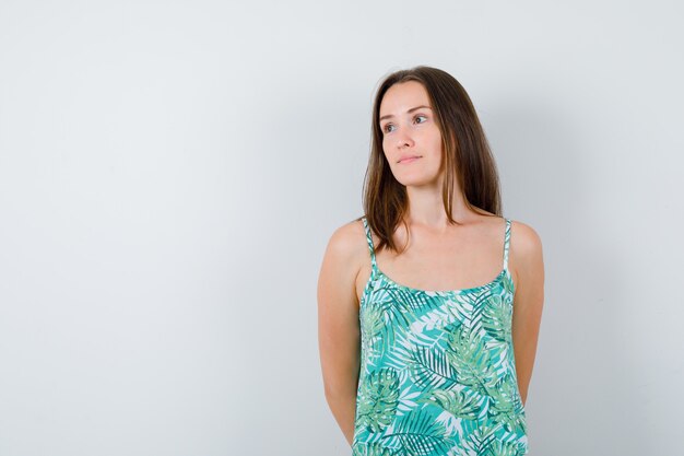 Young lady with hands behind back while looking away and looking thoughtful. front view.