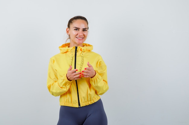 Young lady with hands on chest in yellow jacket and looking merry. front view.
