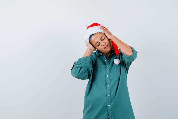 크리스마스 모자, 셔츠를 입고 머리에 손을 얹고 편안하게 보이는 젊은 아가씨.