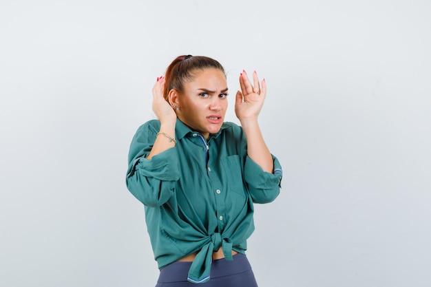 Young lady with hands near head in shirt, pants and looking anxious , front view.