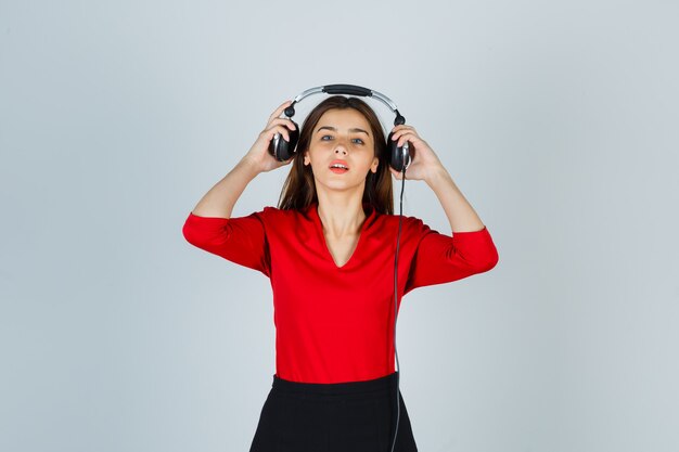 Young lady with headphones posing while standing in red blouse