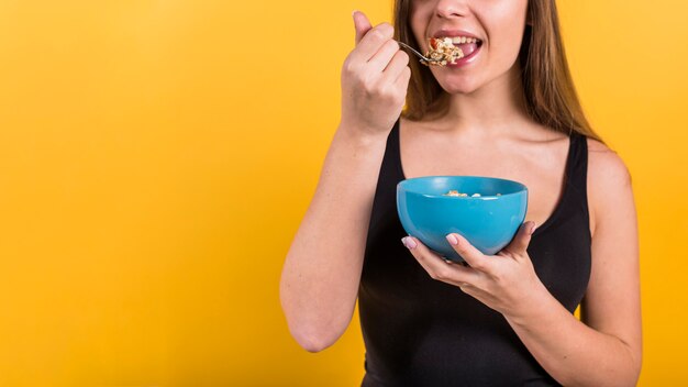 Young lady with spoon and bowl eating flakes